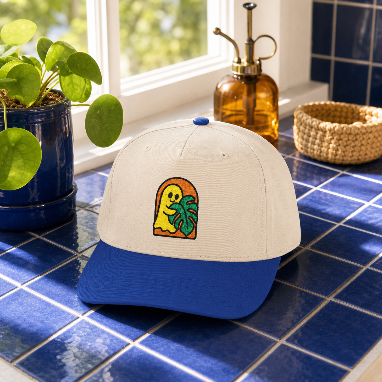 Ghost Monstera embroidered hat, Royal and Natural, in a botanical garden setting
