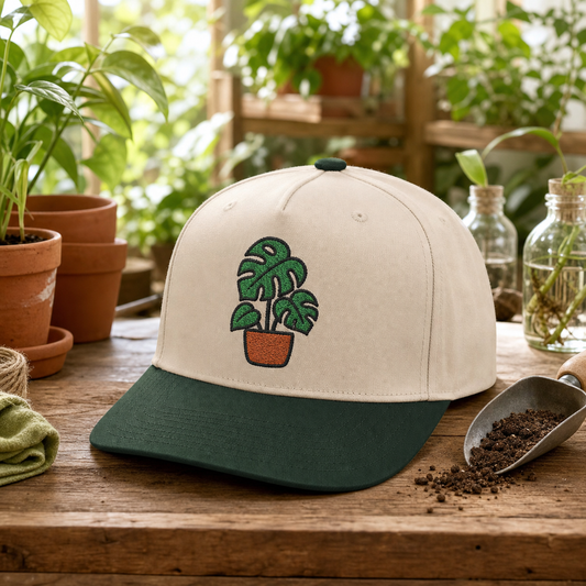 Monstera Mood embroidered hat in Dark Green / Natural on a greenhouse potting bench