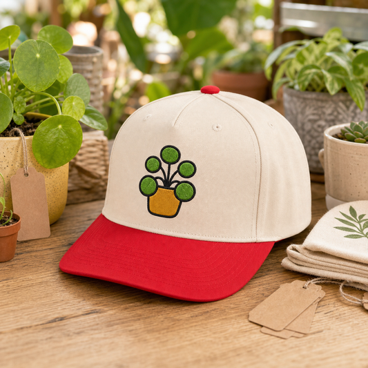 Pilea Party embroidered hat in Red / Natural on a plant swap table