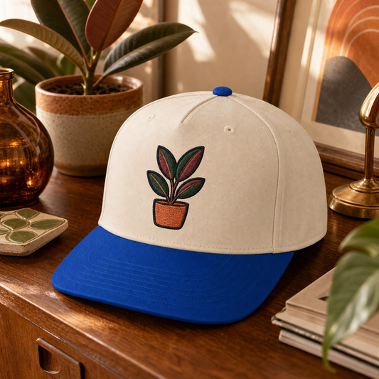 Rubber Plant Pop embroidered hat in Royal / Natural on a vintage plant credenza